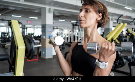 Portrait von athletischen reife Frau macht von reps eingestellte übung für Bizeps mit Hanteln in den Händen in der Turnhalle. Sie ist Hanteln, kopieren. Ausbildung und Sport Konzept. Stockfoto