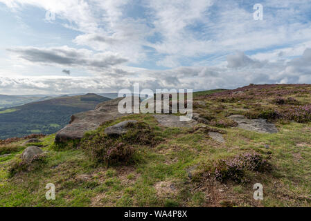 Bamford Kante Blick über Hügel zu gewinnen suchen mit blauer Himmel, flauschige Wolken, und lila Heidekraut im Peak District National Park. Stockfoto