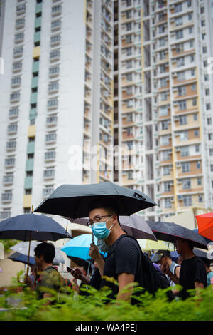 Hongkong, China. 17 Aug, 2019. Die Teilnehmer an einem Protestmarsch durch die Hongkongs Stadtteil Kowloon vor einem Hochhaus, und selbst mit Sonnenschirmen vor dem Regen schützen. In Hongkong gab es massive Proteste für mehr als zwei Monate. Die Demonstrationen wurden durch eine Gesetzesvorlage der Regierung ausgelöst - jetzt in der Warteschleife - Verdacht auf Auslieferung von Verbrechern zu China. Credit: Gregor Fischer/dpa/Alamy leben Nachrichten Stockfoto