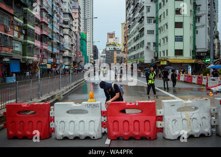 Hongkong, China. 17 Aug, 2019. Ein Teilnehmer in einem Protestmarsch in die Hong Kong Stadtteil Kowloon errichtet Baustelle Barrieren als Blockade auf einer Straße. In Hongkong gab es massive Proteste für mehr als zwei Monate. Die Demonstrationen wurden durch eine Gesetzesvorlage der Regierung ausgelöst - jetzt in der Warteschleife - Verdacht auf Auslieferung von Verbrechern zu China. Credit: Gregor Fischer/dpa/Alamy leben Nachrichten Stockfoto