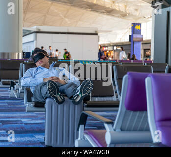 Flughafen Hong Kong, Hong Kong - 29. Oktober 2018: Eine junge Frau schlafen auf einem Sitz auf den Flughafen Hong Kong, ruhen seine Füße auf seinem Koffer. Stockfoto