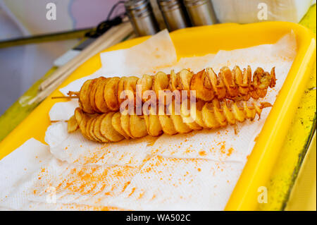 Spirale Kartoffeln gebraten, auf Holzstäbchen, Spirale. Verkauf von Speisen auf dem Markt. Ungesunde frittierten Speisen. Street Food, eine Spirale gebraten Kartoffel auf einem Stock. Pota Stockfoto