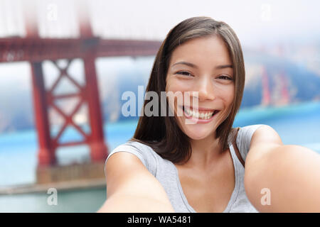 Selfie Mädchen auf San Francisco Golden Bridge reisen. Nette junge asiatische Frau nach der Aufnahme mit Ihrem Smartphone in den Sommerferien vor der berühmten amerikanischen Attraktion, Kalifornien, USA. Stockfoto