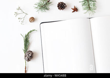 Weihnachten desktop Schreibwaren Mock-up-Szene. Nahaufnahme von Leer notebook. Rahmen von Acorn, Tannenzapfen Tannenzweigen und gypsophila Blumen auf weißem Tabelle Stockfoto