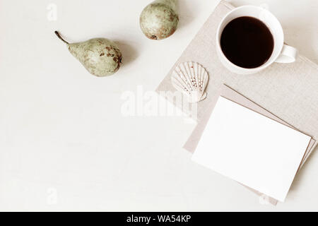 Feminine Schreibwaren, desktop Mock-up-Szene. Leere Grußkarte, Handwerk Umschlag, Tasse Kaffee, sea shell, Birnen und alte Bücher. Weißem Hintergrund Stockfoto