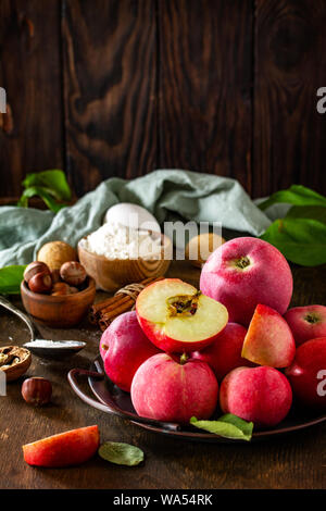 Apple backen saisonale Konzept. Zutaten für Apple Pie (roter Apfel, Mehl, Eier, Anis, Haselnüssen, Zucker und Zimt) auf einem rustikalen Holztisch. Kostenlos Stockfoto