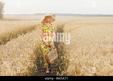 Ein junges Mädchen Spaziergänge entlang eines Pfades in einem Feld gesät mit Gerste. Model posiert in einer stilvollen ländlichen Kleid Stockfoto