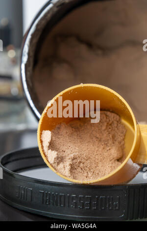 Kunststoff Messlöffel und Haufen brauner Schokolade Protein Pulver. Sport Ernährung Konzept. Stockfoto