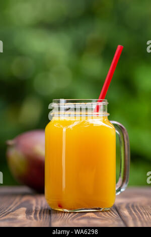 Frische mango Saft im Glas Marmeladenglas mit reifen Früchten auf hölzernen Tisch im Freien. Sommer erfrischendes Getränk Stockfoto