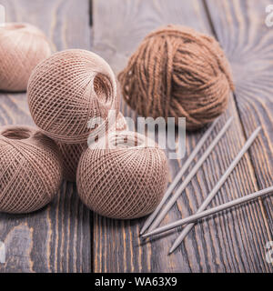 Kugeln von Garn und Stricknadeln zum Stricken auf einer hölzernen Hintergrund Stockfoto