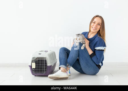 Charmante positive junge Frau hält in ihrer Hände ihre schönen grauen schottischen Katze sitzt auf dem Boden in eine neue Wohnung. Pet-Konzept. Copyspace Stockfoto
