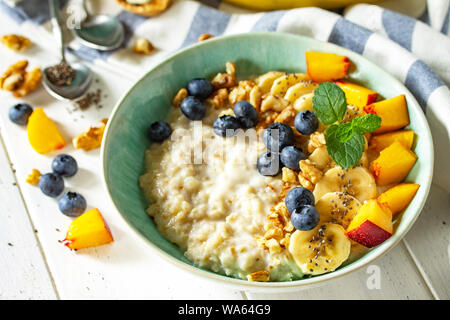 Gesunde Lebensmittel für Frühstück, vegetarisch, vegan, alkiline Ernährung Food Konzept. Haferflocken Porridge mit Chia, Banane und Heidelbeeren auf Obst und Nüsse auf ein wh Stockfoto