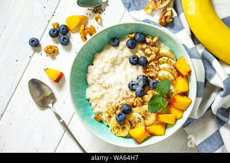 Gesunde Lebensmittel für Frühstück, vegetarisch, vegan, alkiline Ernährung Food Konzept. Haferflocken Porridge mit Chia, Banane und Heidelbeeren auf Obst und Nüsse auf ein wh Stockfoto