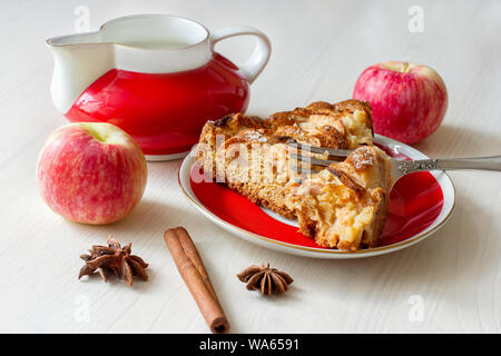 Ein Stück frischen Apfelkuchen auf dem Teller mit Gabel, frische Äpfel, Gewürze und Milchkännchen Nahaufnahme Stockfoto
