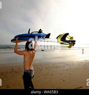 Ein junger Mann sein Surfbrett trägt auf seinem Kopf den Blick in das Meer zu Fuß mit der Abendsonne glühende Hell über Compton Strand Stockfoto