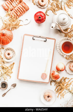 Schöne Herbst flach mit leeren Zwischenablage und Stift auf weißem Desktop mit Kürbis, Granatapfel, Äpfel, Kaffee, Donuts, Gebäck und Blumen. Top vie Stockfoto