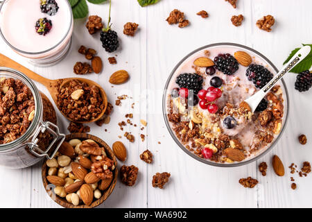 Müsli knusprig Honig Müsli mit Joghurt, frische Beeren, Schokolade und Nüsse in einer Schüssel gegen einen hellen Hintergrund, gesundes Essen, Nahaufnahme, horiz. Stockfoto