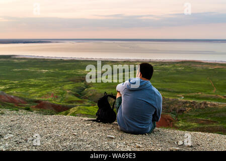 Junge Reisende Mann bei Sonnenuntergang. Touristen sitzen auf dem Hügel über dem See. Stockfoto