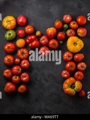 Buchstabe M mit reifen Tomaten auf einem schwarzen Hintergrund, kreative Flach gesundes Essen Konzept. Stockfoto