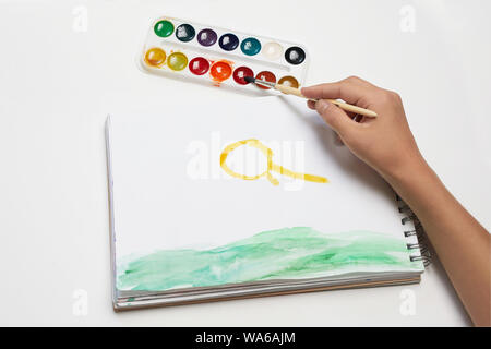 Hand hält eine Bürste in Farben, Kind Zeichnung auf einem weißen Hintergrund Stockfoto