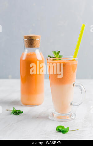 Frische Karotten Saft mit hafermilch und Minze. Vegetarische Getränk für gesundes Essen in einem durchsichtigen Glas auf einem hellen Hintergrund der Seite. Stockfoto