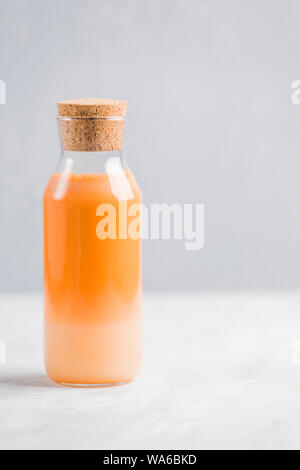 Frische Karotten Saft mit hafermilch und Minze. Vegetarische Getränk für gesundes Essen in eine durchsichtige Flasche mit einem hölzernen Anschlag auf einem hellen Hintergrund nach oben v Stockfoto