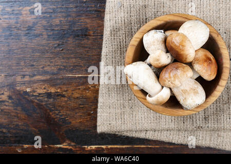 Rohen Steinpilzen in einer Platte auf einem braunen Holz- Hintergrund. Die Platte ist auf eine Serviette von sackleinen Stockfoto