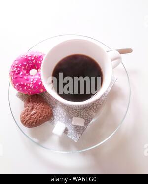 Nahaufnahme einer weißen Keramikkaffeetasse auf einem Teller Mit rosa Donut und herzförmigem Keks Stockfoto