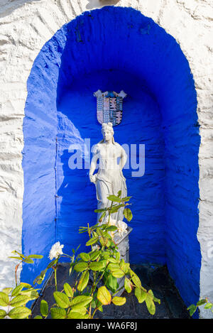 Penrhyndeudraeth, Wales, Großbritannien - 15.August 2019: das antike Griechenland inspiriert Statue auf einem leuchtend kobaltblauen Hintergrund in Portmeirion Stockfoto