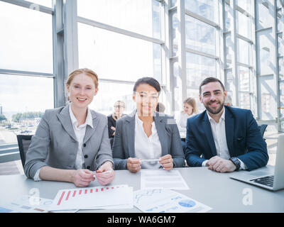 Drei Lächeln Geschäft Leute an Konferenztisch mit Berichten. Business Meeting- und Kommunikationskonzept Stockfoto