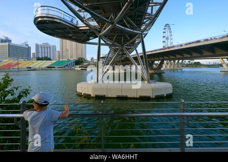 Ein Junge steht unter dem ikonischen Helix Bridge in Singapur, an der Marina Bay mit Blick auf die Marina Square, Singapore Flyer im b/g (r) Stockfoto