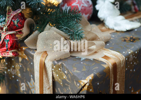 Nahaufnahme eines schön verpackt und mit einer Gold lace ribbon Geschenk unter dem Weihnachtsbaum, selektiver Fokus gebunden Stockfoto