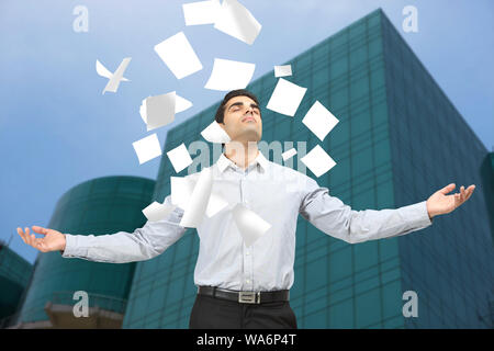 Papiere, die auf einen Geschäftsmann fallen, der mit ausgestreckten Armen steht Stockfoto