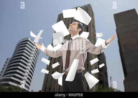 Papiere, die auf einen Geschäftsmann fallen, der mit ausgestreckten Armen steht Stockfoto
