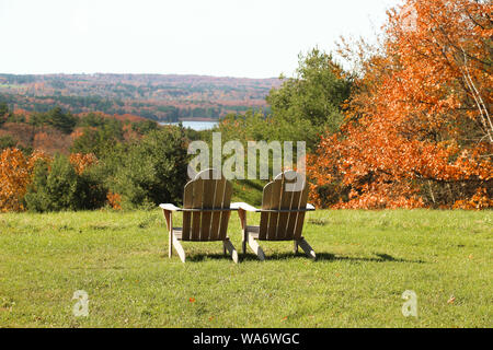 Holz- Adirondack Stühlen mit Blick auf einen schönen Herbst Blick auf den See und die Berge. Stockfoto