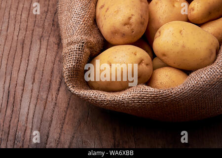 Blick auf den Stapel der neuen Kartoffeln mit Jute Tasche auf Holztisch. Stockfoto