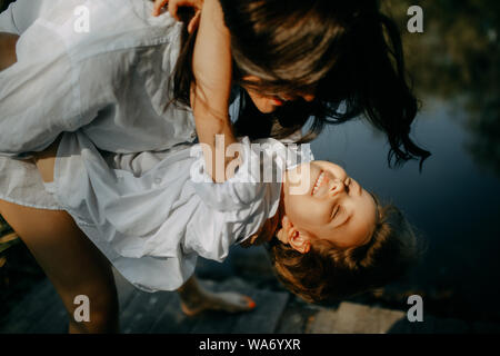 Mutter und Tochter spielen und Spaß haben auf einer Holzbrücke in der Nähe eines kleinen Flusses. Nahaufnahme. Stockfoto