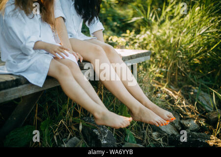 Die Beine der Frau und Kind sind auf dem Hintergrund einer alten Bank und Gras. Nahaufnahme. Stockfoto