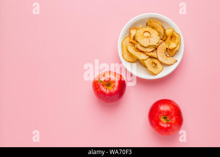 Getrocknete äpfel Chips in weißer Keramik Schüssel mit Frische rote Äpfel auf rosa Hintergrund Stockfoto