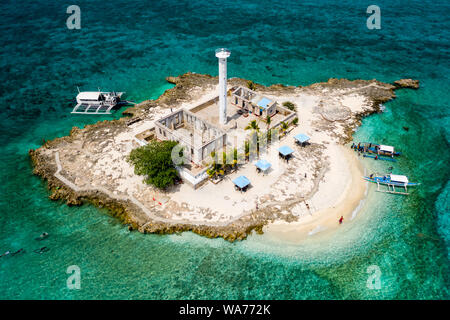 Antenne drone Ansicht der traditionellen Boote neben einer kleinen tropischen Insel mit einem Leuchtturm, von Korallenriff umgeben (Capitancillo Island, Philippinen) Stockfoto