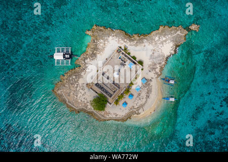 Antenne drone Ansicht der traditionellen Boote neben einer kleinen tropischen Insel mit einem Leuchtturm, von Korallenriff umgeben (Capitancillo Island, Philippinen) Stockfoto