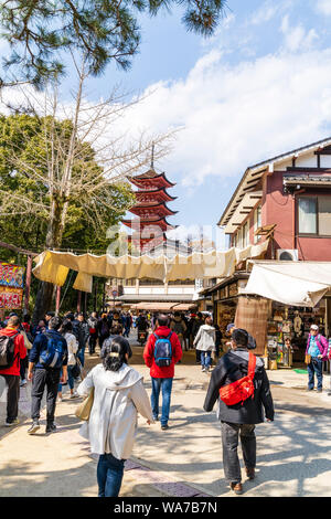 Japan, Miyajima. Blick entlang der Haupteinkaufsstraße mit Ständen und Geschäften auf beiden Seiten, besetzt mit Touristen. Rot 5 stöckige Pagode im Hintergrund. Stockfoto