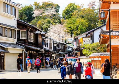 Japan, Miyajima. Touristen in der Einkaufsstraße mit vielen traditionellen Stil Geschäfte und Läden, die mit dem Errichten der Itsukushima-schrein auf der rechten Seite. Stockfoto