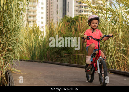 Kleines Mädchen auf dem Fahrrad entlang einem Weg außerhalb der Stadt mit Helm und Schutzausrüstung Stockfoto