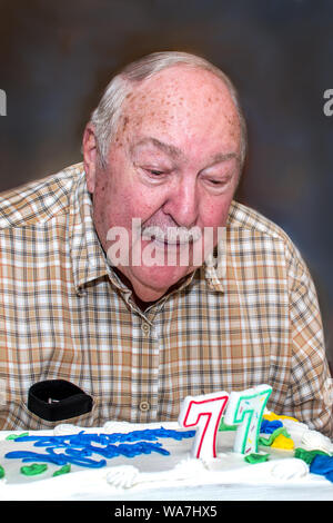 Ein älterer Mann bläst die Kerzen auf dem Kuchen für seinen 77. Geburtstag Stockfoto