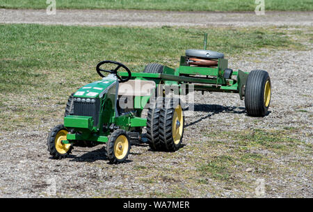 Eine kleine grüne Trettraktor für Kinder, ist mit schweren Gewichten in einem altmodischen Traktor ziehen gewichteten Stockfoto