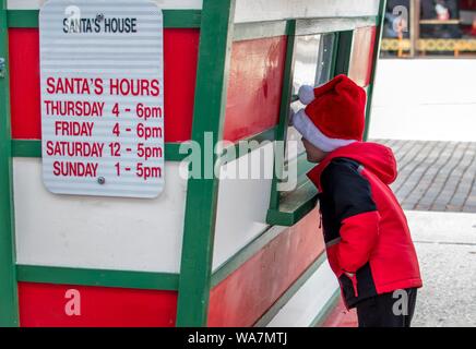 Kleiner Junge trägt eine Santa hat, sieht durch das Fenster, um zu sehen, ob Santa Es ist innen Stockfoto