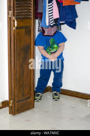 Ein kleiner Junge spielt Verstecken und Suchen von versteckt sich im Schrank hinter Bekleidung Stockfoto