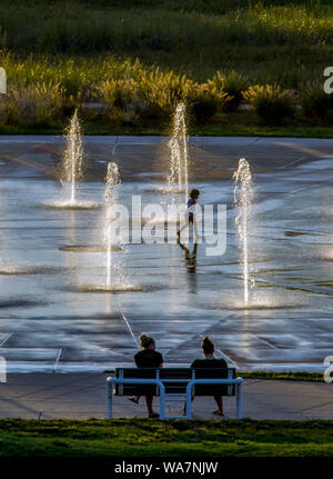 Erwachsene sehen Sie ein laufendes Kind glücklich in einem Brunnen bei Sonnenuntergang spielen Stockfoto