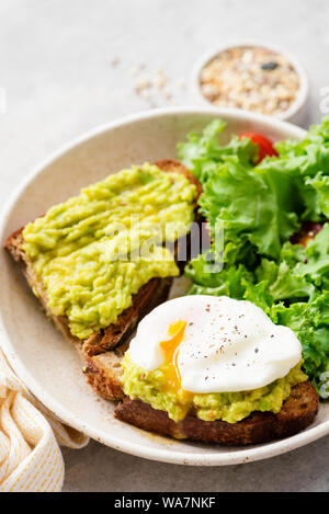 Avocado und pochiertem Ei auf geröstetem Schwarzbrot serviert mit Grünkohl und Tomatensalat. Detailansicht für gesunde Ernährung Stockfoto